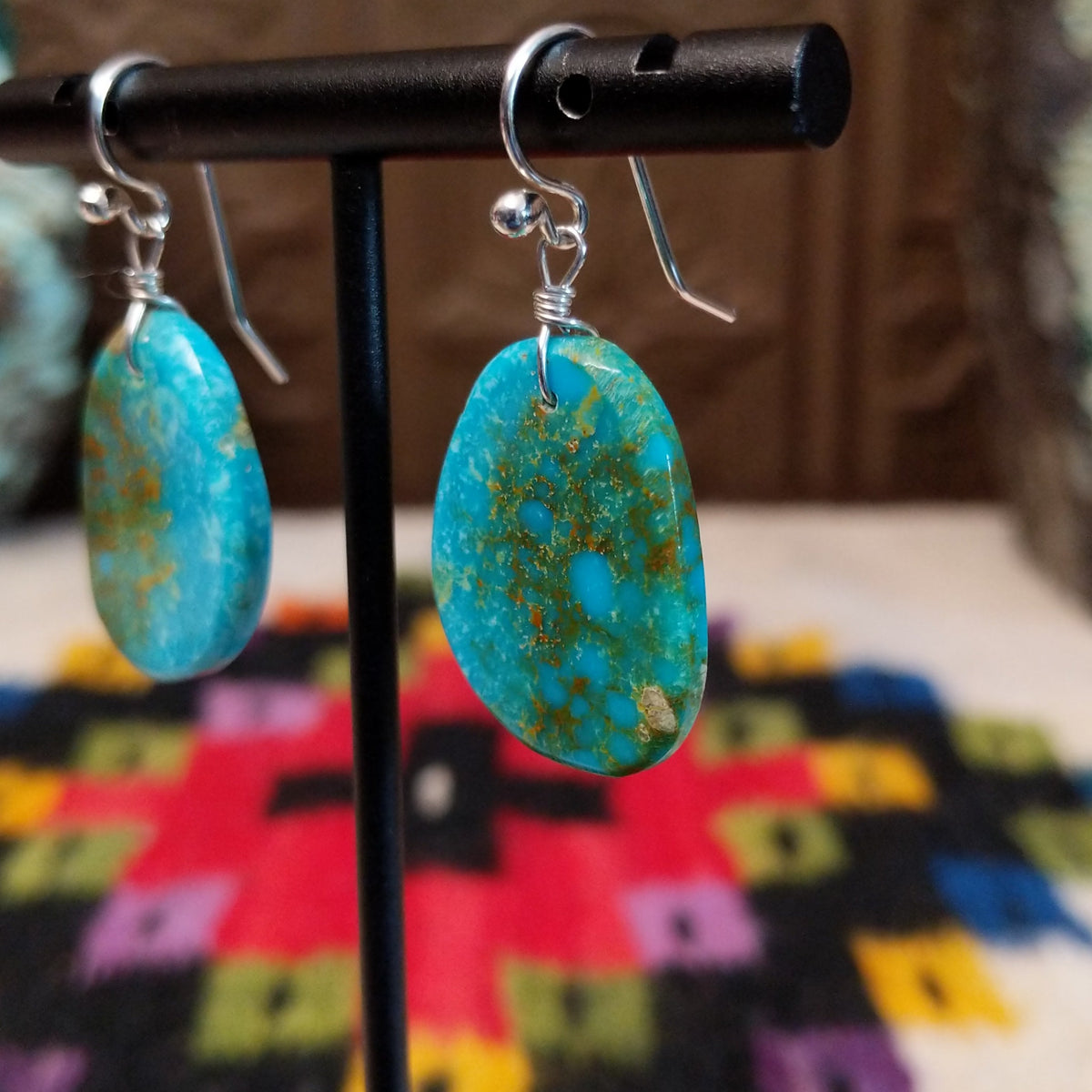 Blue-Green Turquoise Slab Earrings by Ronald Chavez featuring freeform blue-green turquoise stones with natural golden-brown matrix, suspended from silver hooks; side view.