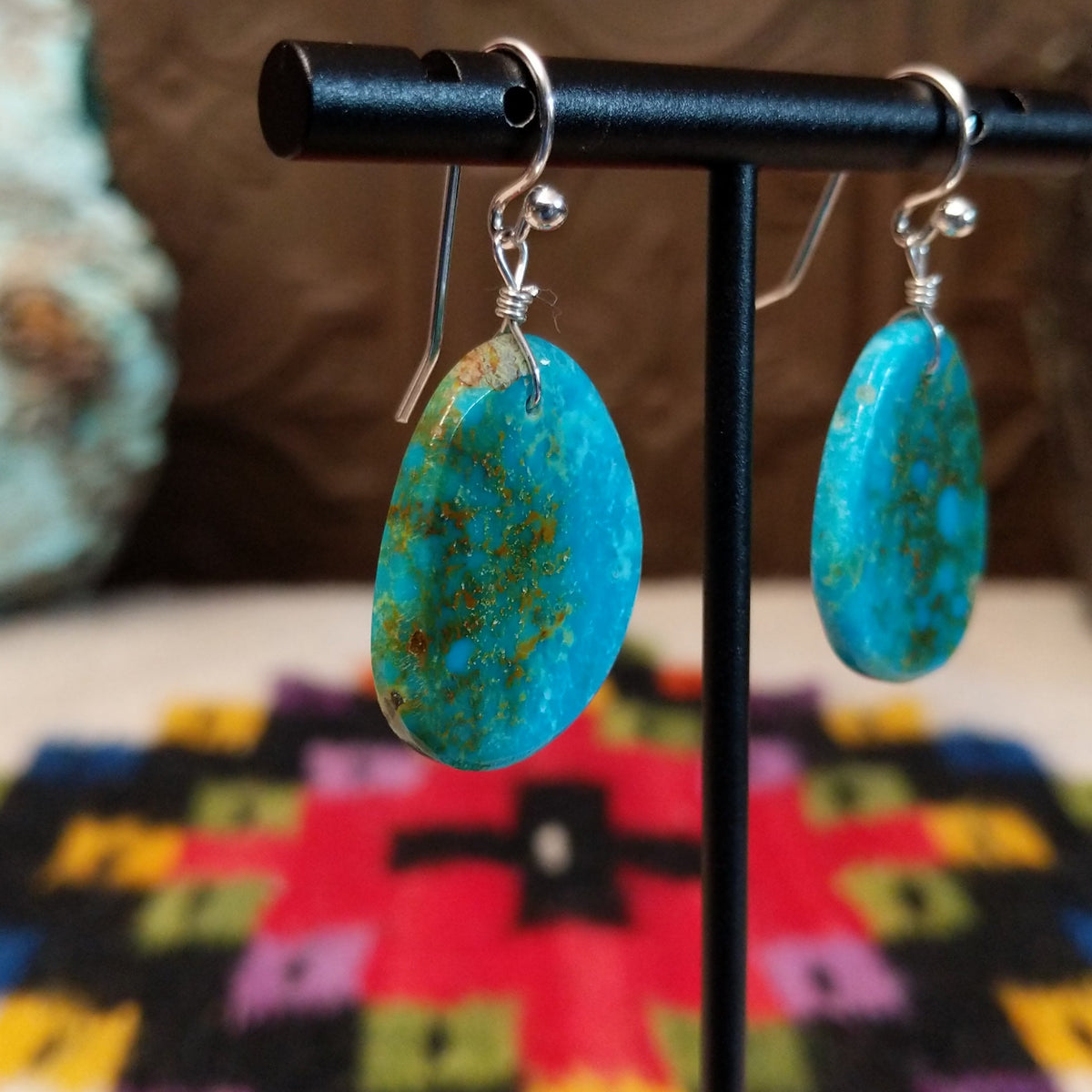 Blue-Green Turquoise Slab Earrings by Ronald Chavez featuring freeform blue-green turquoise stones with natural golden-brown matrix, suspended from silver hooks; side view.