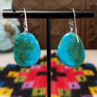 Blue-Green Turquoise Slab Earrings by Ronald Chavez featuring freeform blue-green turquoise stones with natural golden-brown matrix, suspended from silver hooks; backside view.