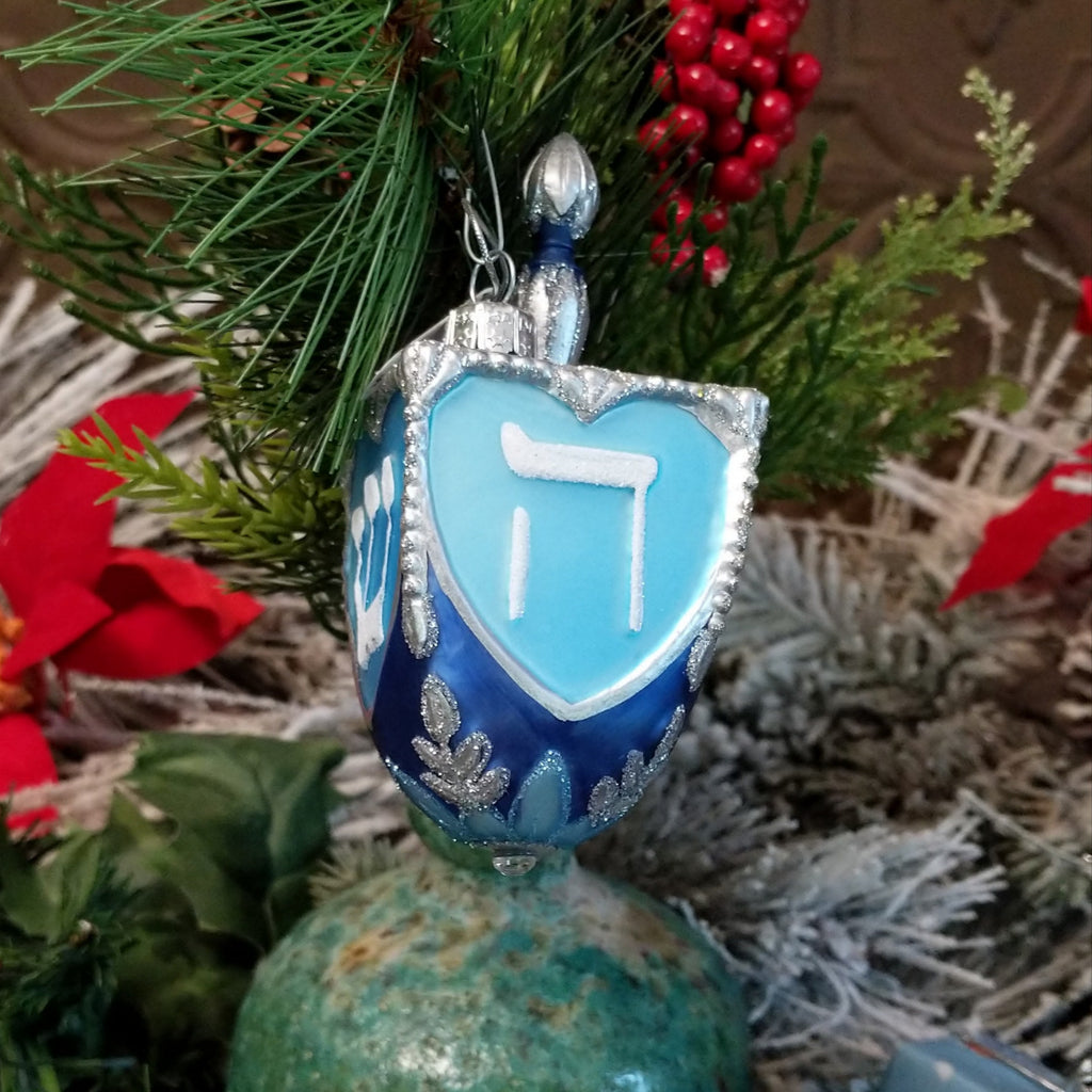 Glass made into a dreidel and painted in various blues, silver, and white with traditional symbols on its form.