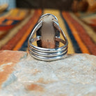 Blue Manmade Opal Ring by Terry Wood featuring an elongated oval blue opal with iridescent tones, decorative stamped sterling silver bezel, raised silver beads, and split-shank band; underside view.