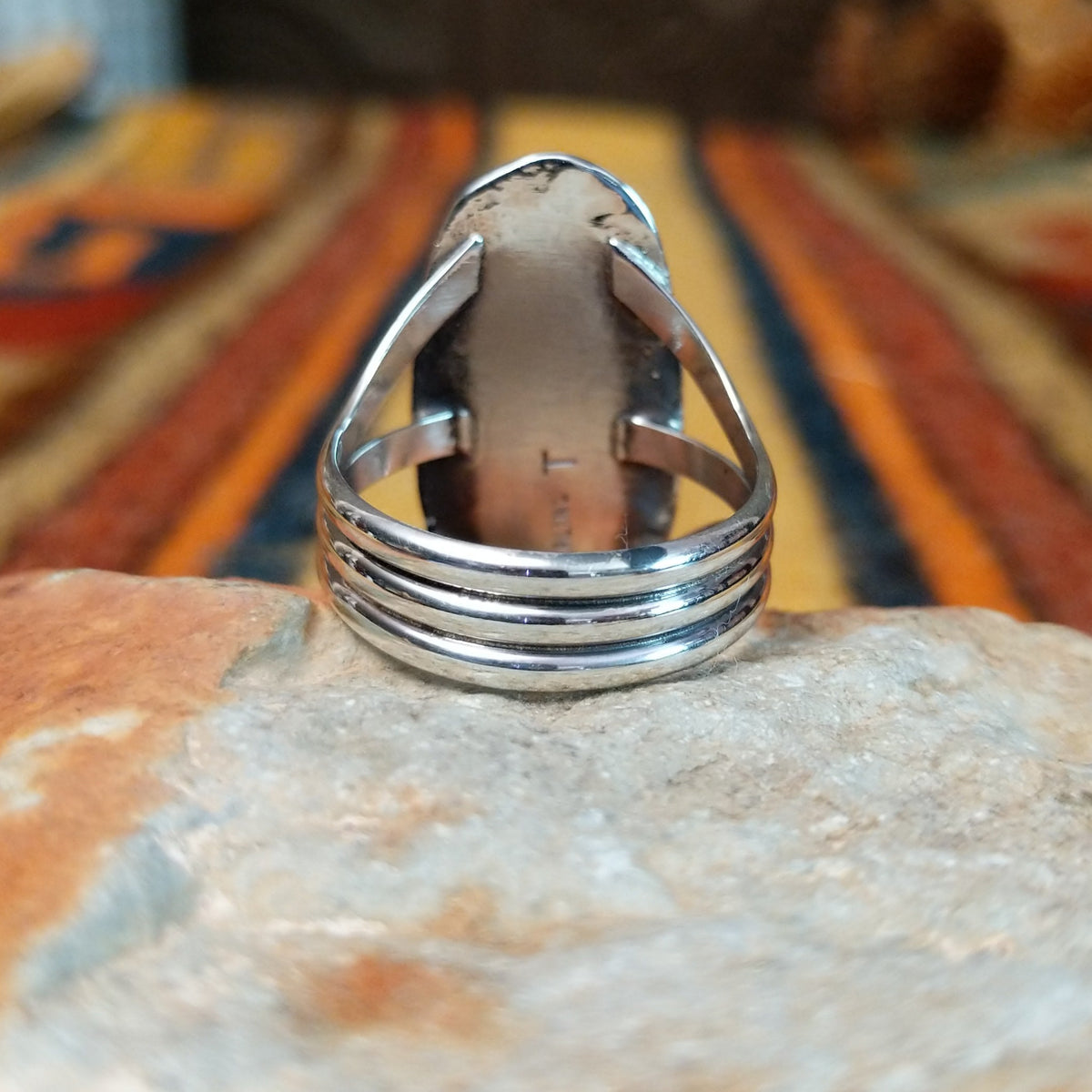 Blue Manmade Opal Ring by Terry Wood featuring an elongated oval blue opal with iridescent tones, decorative stamped sterling silver bezel, raised silver beads, and split-shank band; underside view.