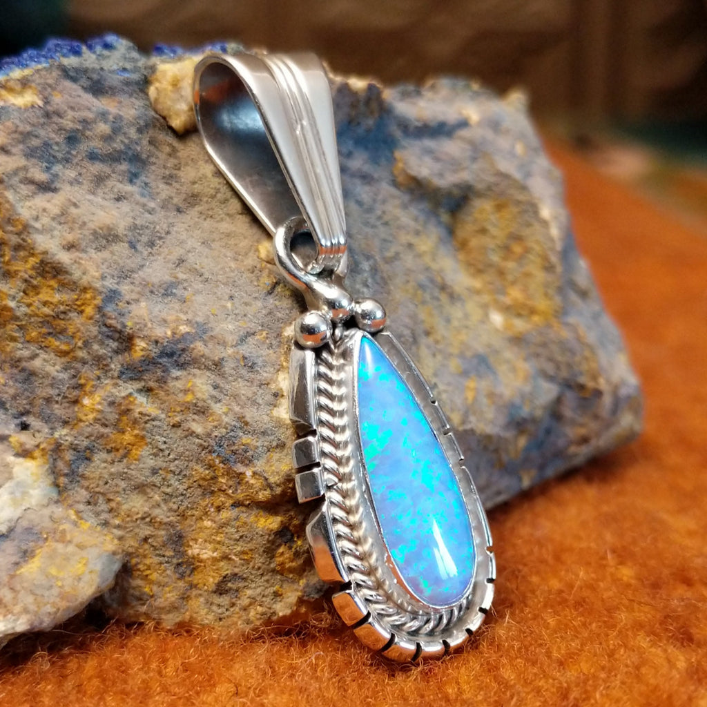 Teardrop-shaped blue man-made opal set in sterling silver with twisted rope and intricate incisions on the frame.