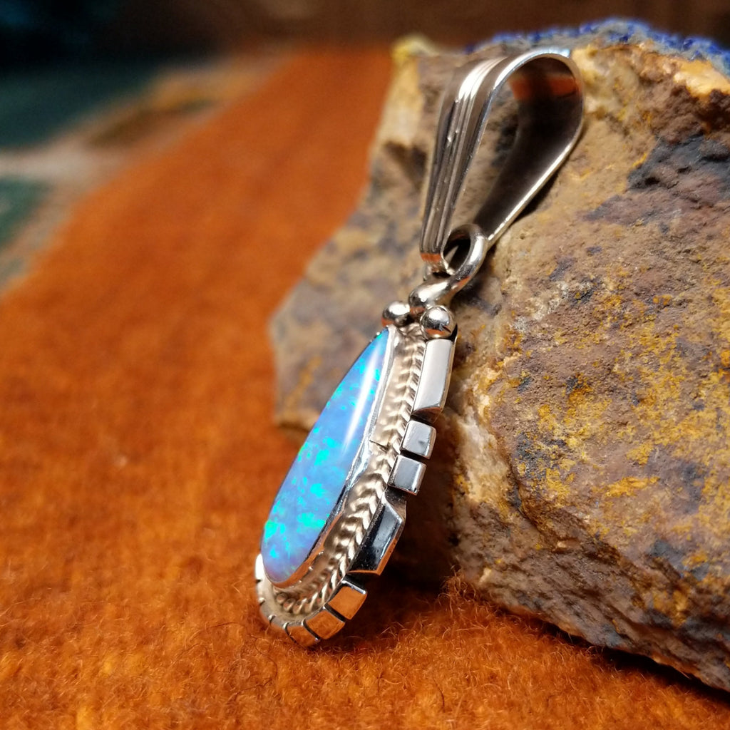 Teardrop-shaped blue man-made opal set in sterling silver with twisted rope and intricate incisions on the frame.