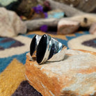 Handcrafted Navajo sterling silver ring by Ann Curley featuring three graduated oval black onyx cabochons in bezel settings with polished silver bead accents on a wide statement band; side view.