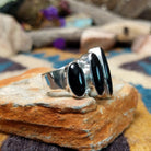 Handcrafted Navajo sterling silver ring by Ann Curley featuring three graduated oval black onyx cabochons in bezel settings with polished silver bead accents on a wide statement band; side view.