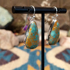 Handcrafted sterling silver teardrop earrings by Lowell Draper featuring natural Boulder Turquoise with vibrant blue coloring and golden-brown matrix on French hooks; side view.