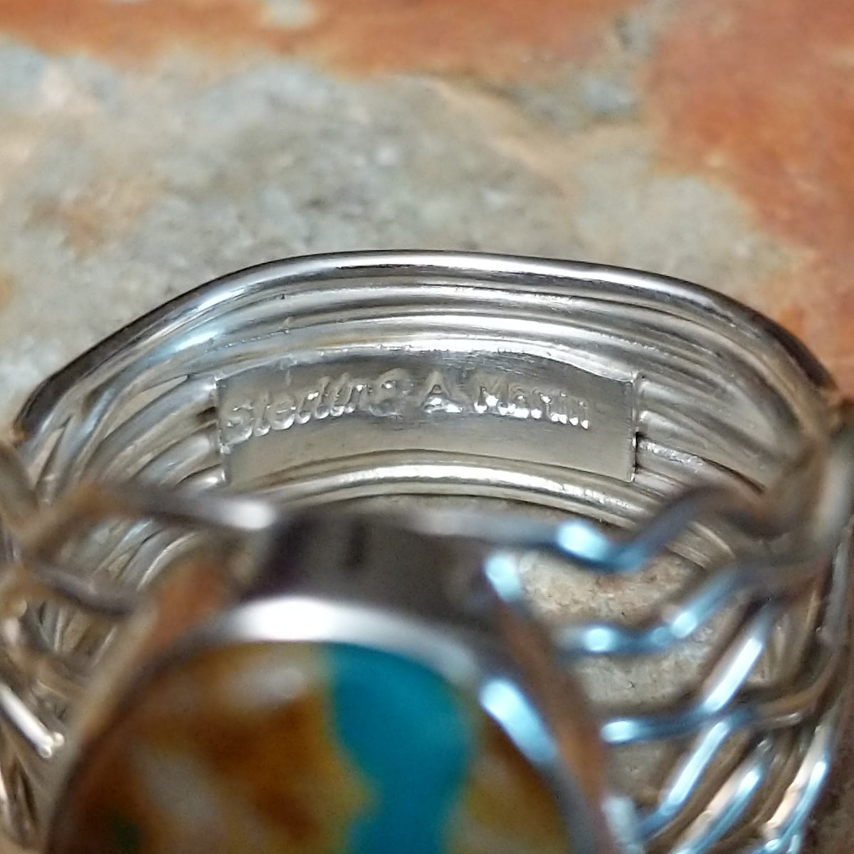 Boulder Turquoise Strand Ring by Angela Martin featuring a natural turquoise stone set in sterling silver, size 8, approximately 0.75 inches long and 0.875 inches wide. Handcrafted jewelry piece with distinctive turquoise patterns; artisan and Sterling Silver stamp.