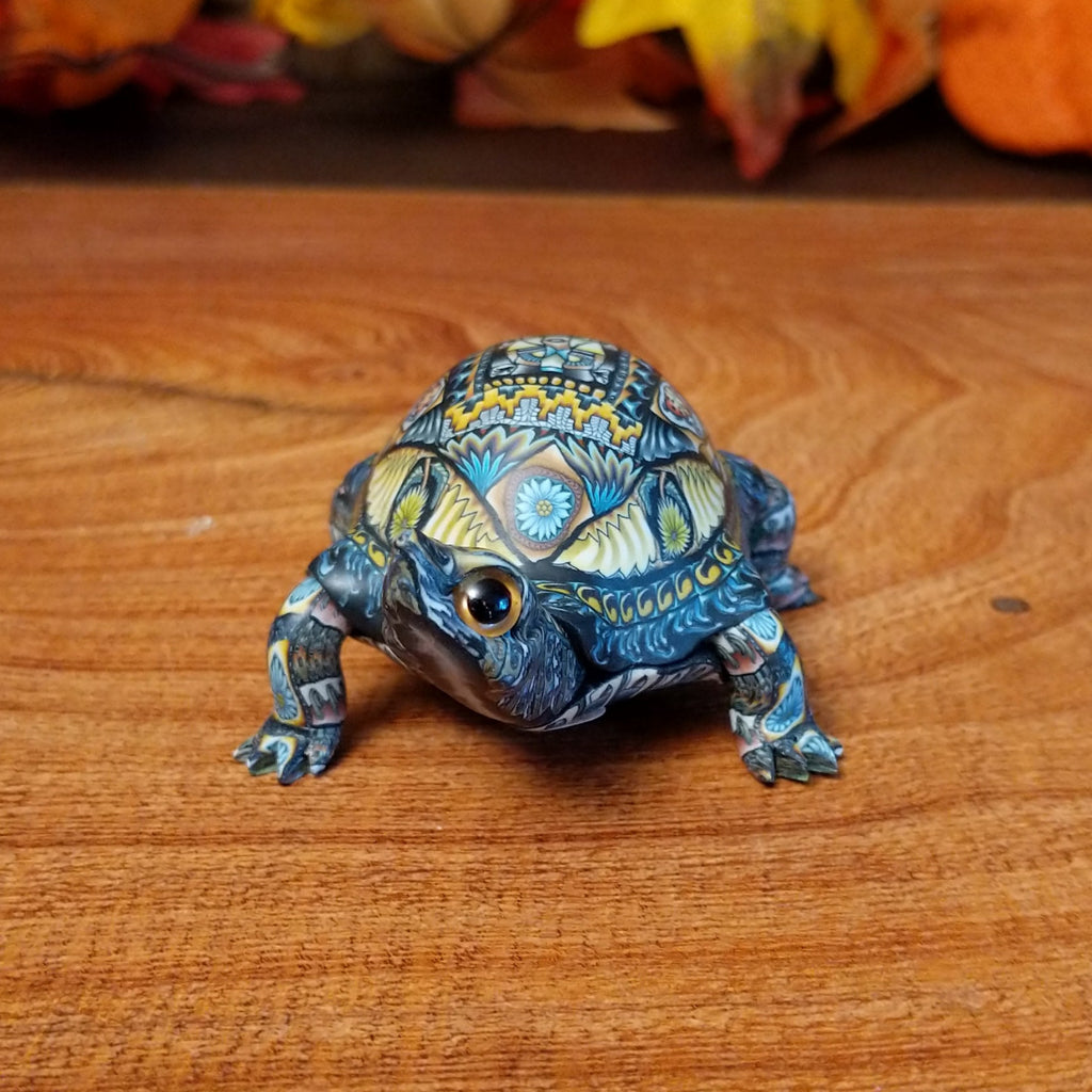 Polymer clay used to create a detailed box turtle with vibrant insect and floral motifs.