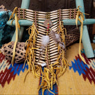 Breastplate artifact reproduction by Linda Lee featuring bone hairpipe beads, leather fringe, brass-toned beads, and feather accents.