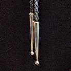 This striking Bumblebee Jasper Bolo Tie by Terry Wood features a bright yellow oval stone with gray and black matrix, a decorative stamped silver setting, braided black leather cord, and polished silver tips; tips close-up view.