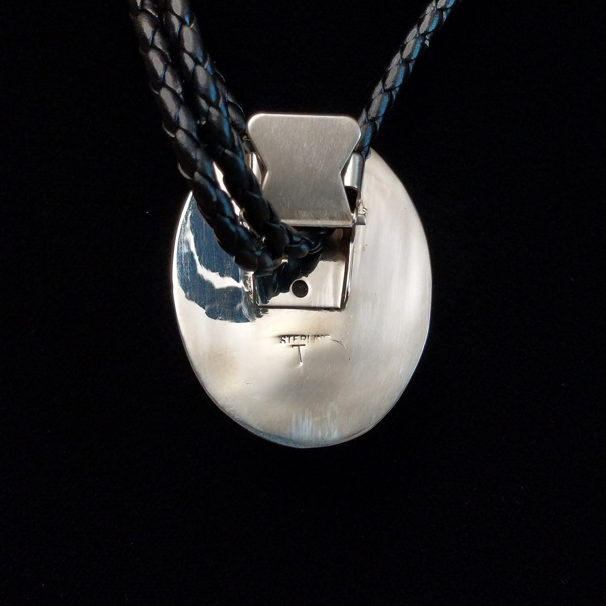 This striking Bumblebee Jasper Bolo Tie by Terry Wood features a bright yellow oval stone with gray and black matrix, a decorative stamped silver setting, braided black leather cord, and polished silver tips; artisan and Sterling Silver stamp on back.