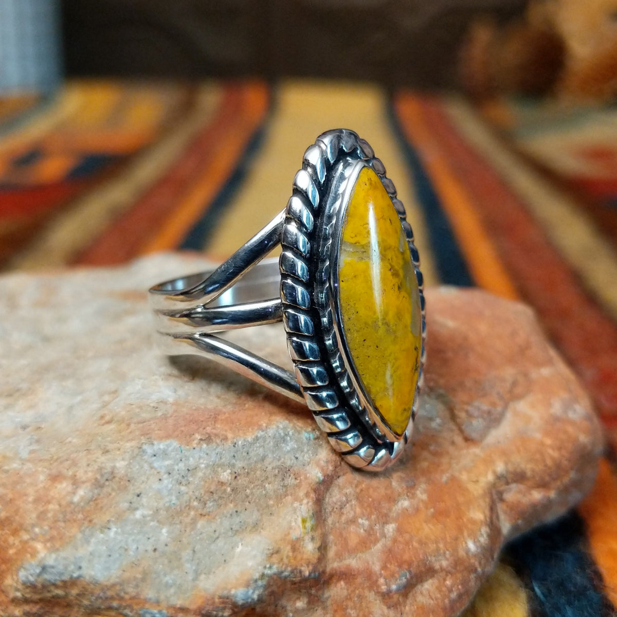 This striking Bumblebee Jasper Navette Ring by Amory Begay features an elongated golden-yellow stone with natural matrix, surrounded by a scalloped silver border and an open split-shank band; side view.