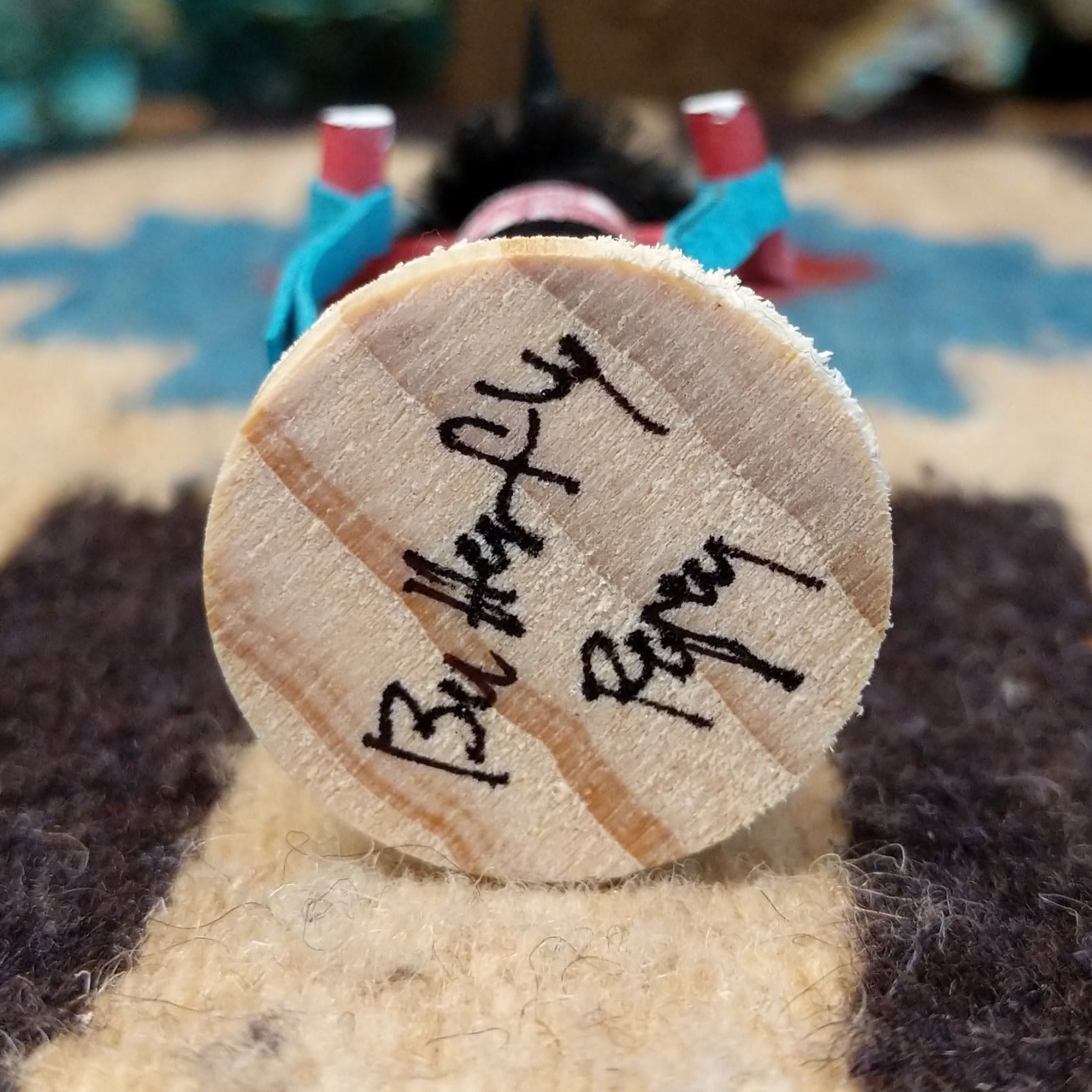 Underside of mini butterfly kachina doll showing handwritten signature and label on wood base.