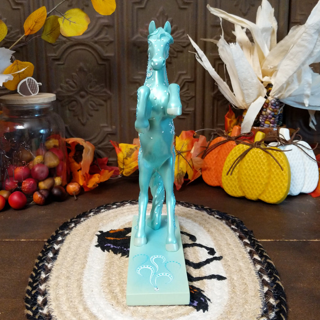 Resin pony painted a shimmering teal with squalls and snowflakes decorating its body.