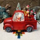 Red Christmas truck snow globe with Santa in the cab and four dogs wearing Santa hats in the truck bed.