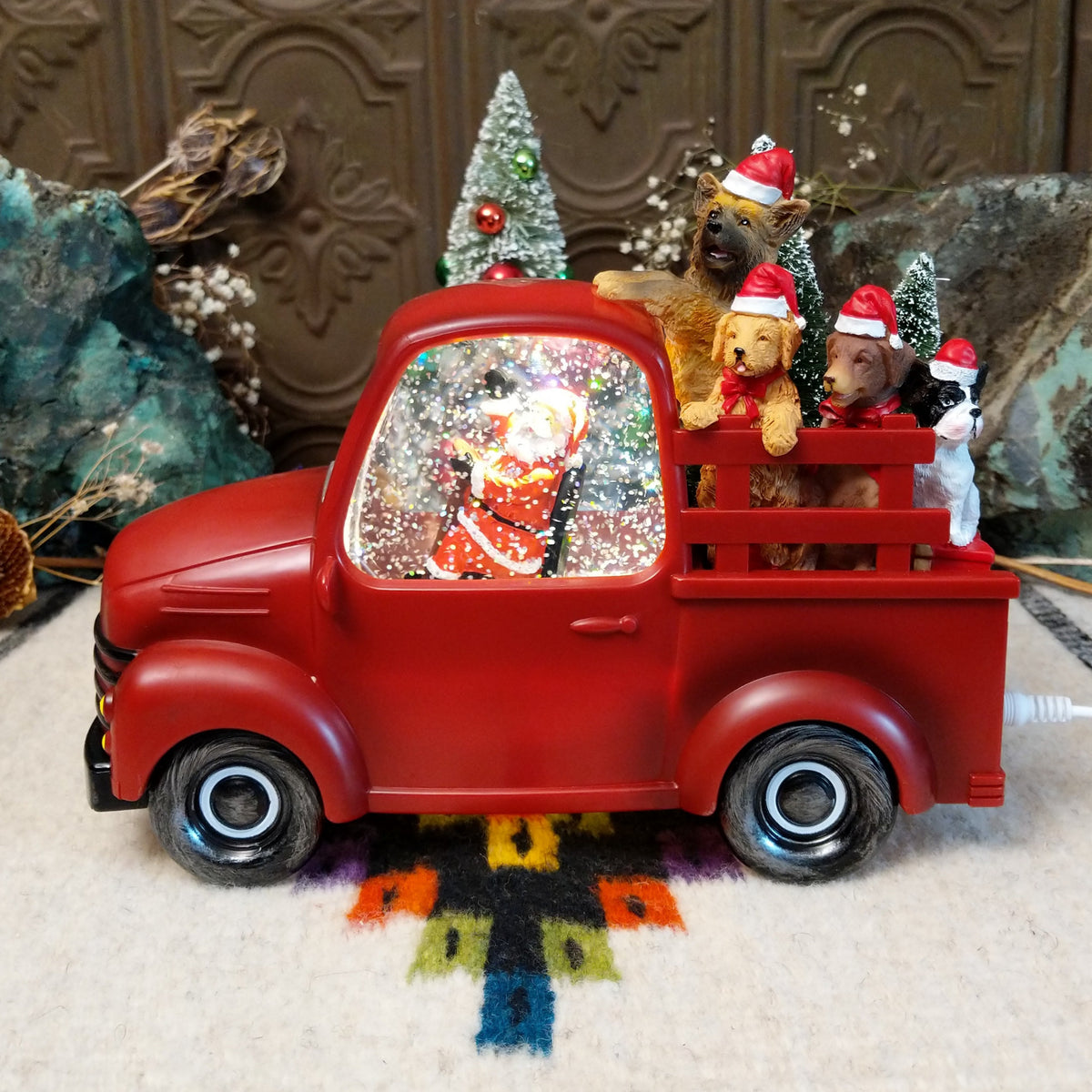 Red Christmas truck snow globe with Santa in the cab and four dogs wearing Santa hats in the truck bed.