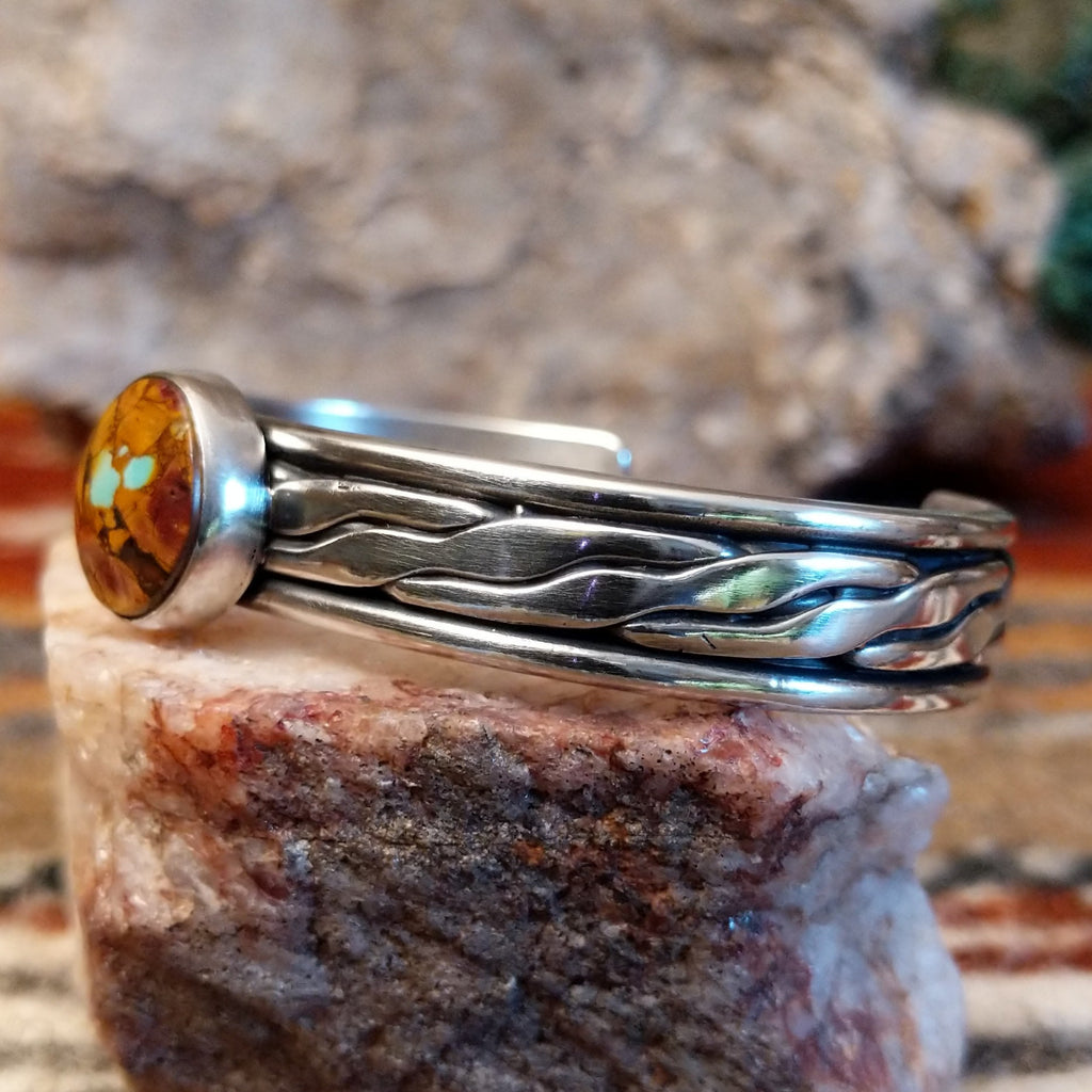 Silver bracelet with a circular stone of Boulder Turquoise on a silver surface, side view