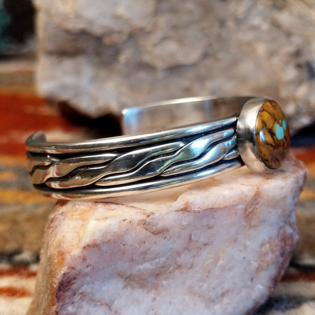 Silver bracelet with a circular stone of Boulder Turquoise on a silver surface, side view