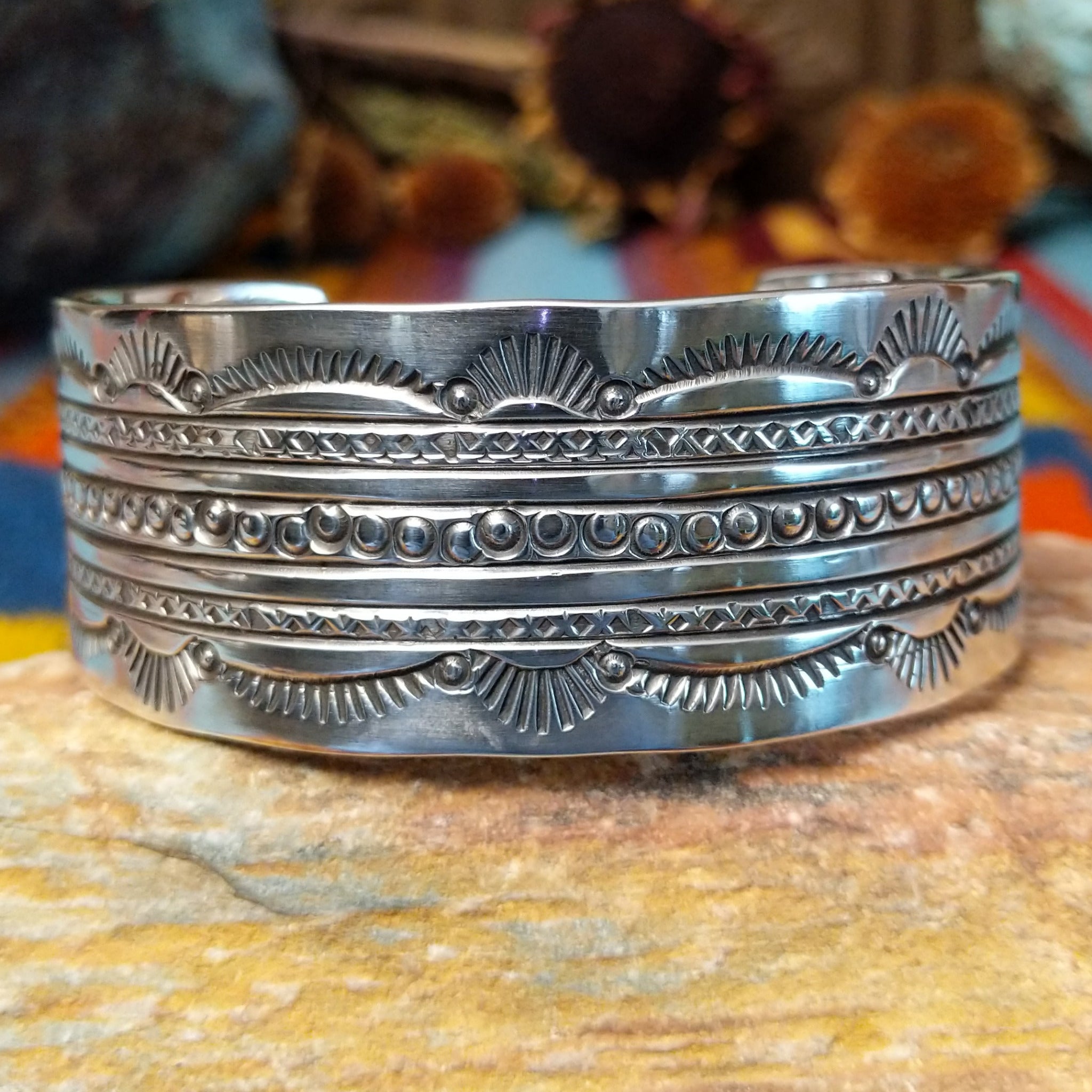 Wide silver cuff by Charlene and Robert Little with layered rows of sunburst, diamond, and circle stampwork.