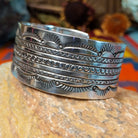 Wide silver cuff by Charlene and Robert Little with layered rows of sunburst, diamond, and circle stampwork.