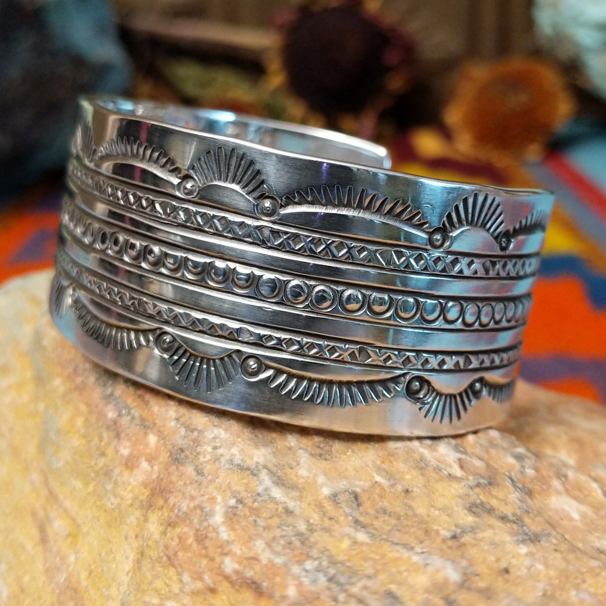 Wide silver cuff by Charlene and Robert Little with layered rows of sunburst, diamond, and circle stampwork.