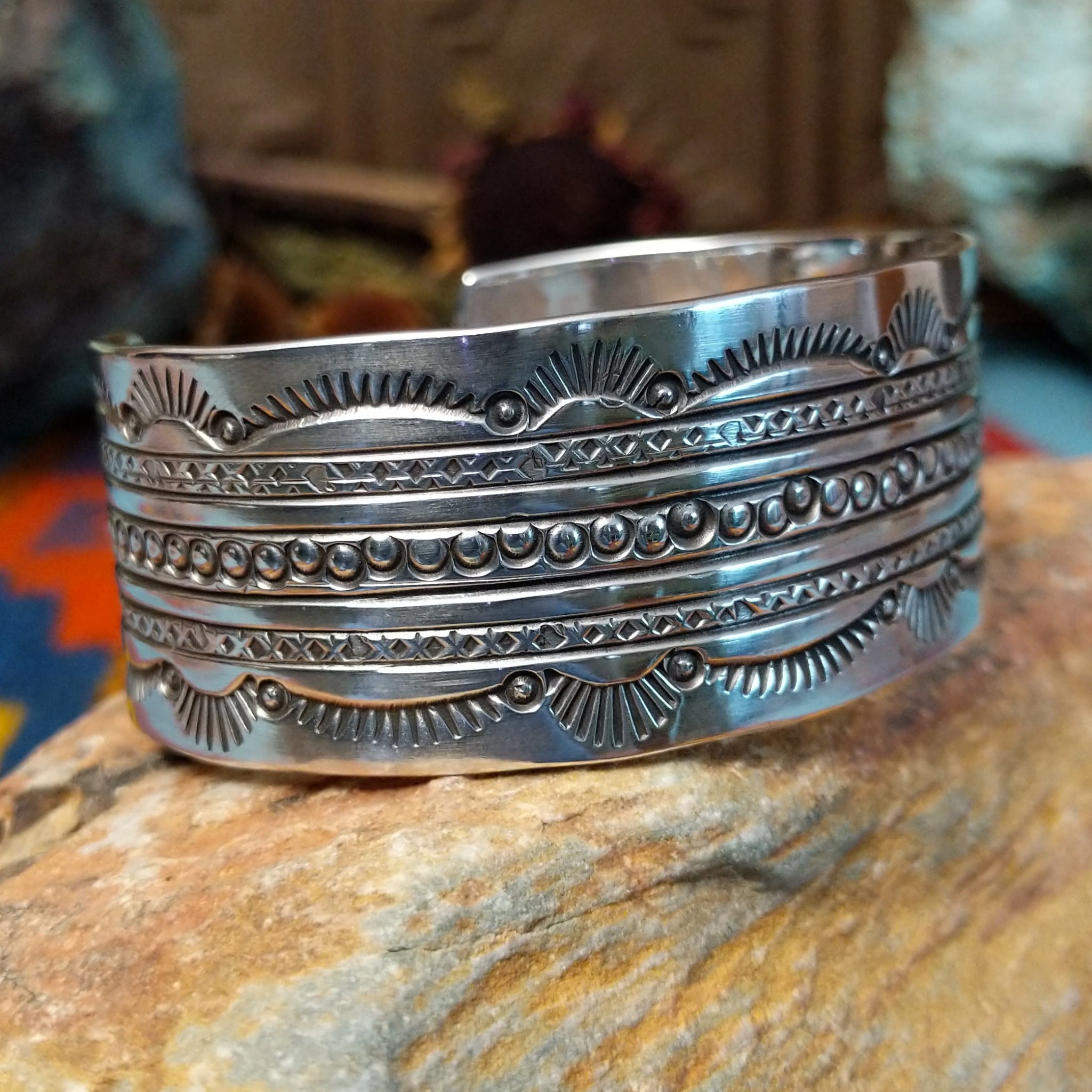 Wide silver cuff by Charlene and Robert Little with layered rows of sunburst, diamond, and circle stampwork.