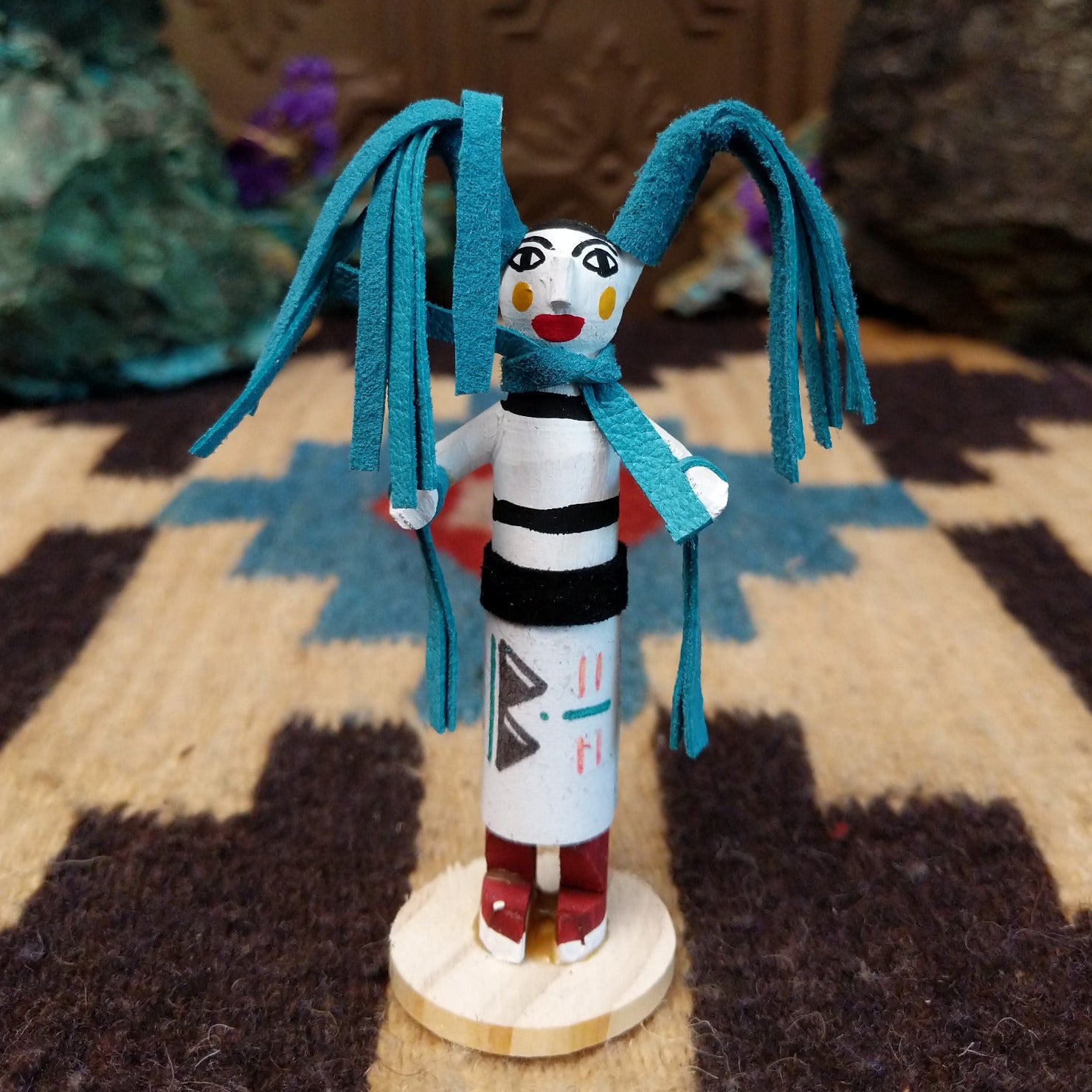 Mini clown kachina by Rosalind Grey with turquoise pigtails, white face, black striped body, and white geometric-patterned garment.