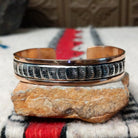 Copper and silver cuff by Robert Little featuring a repeating stamped bush-inspired pattern with oxidized detailing, framed by polished copper borders.
