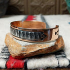 Copper and silver cuff by Robert Little featuring a repeating stamped bush-inspired pattern with oxidized detailing, framed by polished copper borders; side view.