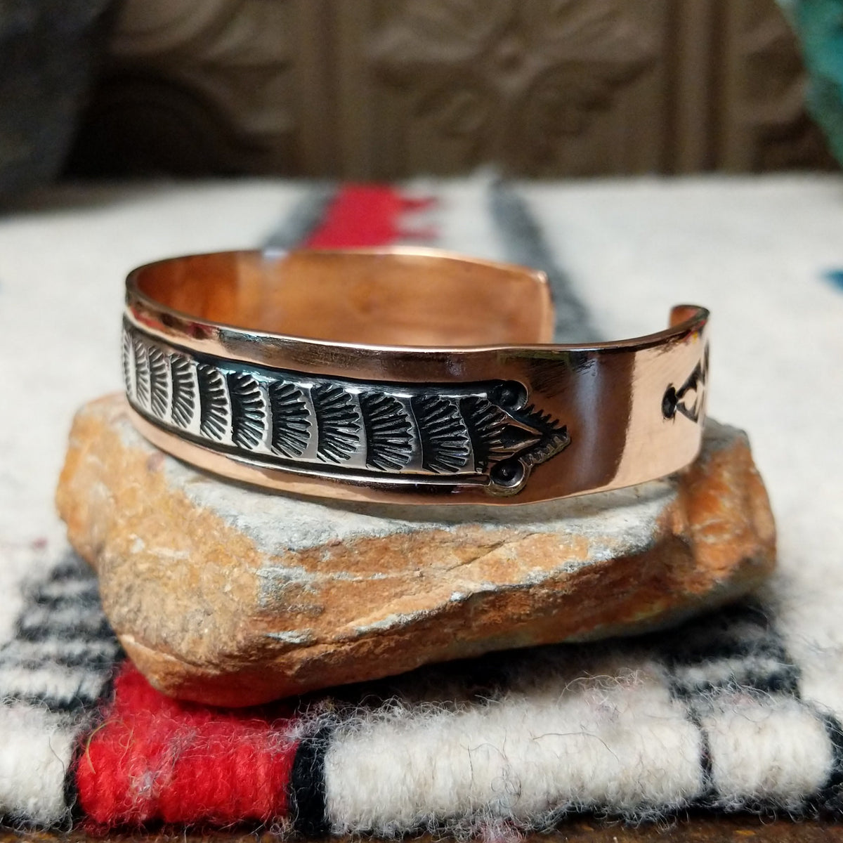 Copper and silver cuff by Robert Little featuring a repeating stamped bush-inspired pattern with oxidized detailing, framed by polished copper borders; side view.