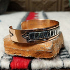 Copper and silver cuff by Robert Little featuring a repeating stamped bush-inspired pattern with oxidized detailing, framed by polished copper borders; side view.