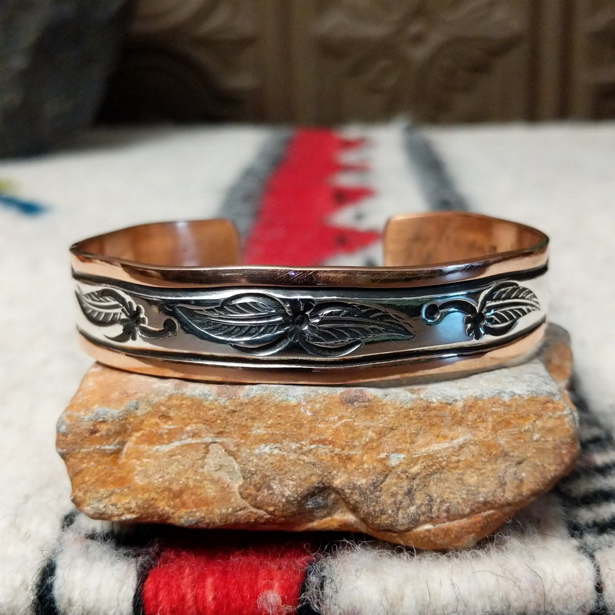 This Copper & Silver Feather Cuff by Robert Little features polished copper borders and a sterling silver center decorated with detailed feather motifs, curved accents, and dark oxidized stamping.