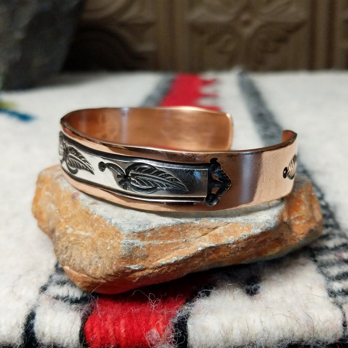This Copper & Silver Feather Cuff by Robert Little features polished copper borders and a sterling silver center decorated with detailed feather motifs, curved accents, and dark oxidized stamping; side view.