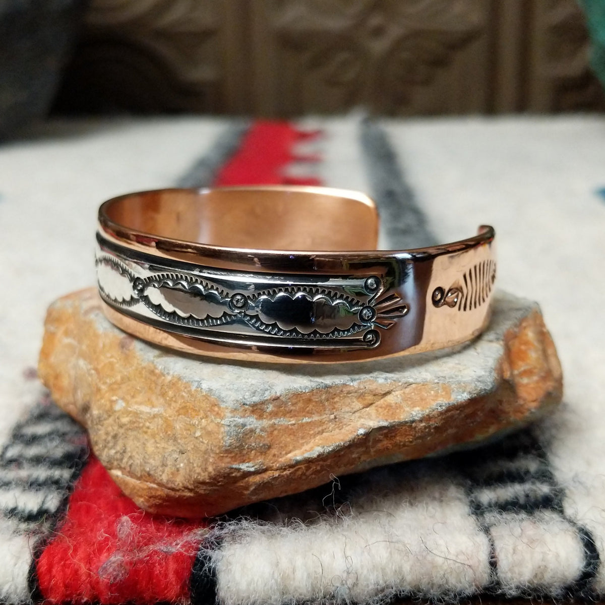 This Copper & Silver Cuff by Robert Little features polished copper borders, a sterling silver center, repeating scalloped hand-stamped motifs, fine textured edges, and dark oxidized accents; side view.