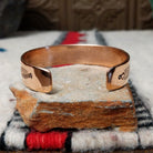 This Copper & Silver Cuff by Robert Little features polished copper borders, a sterling silver center, repeating scalloped hand-stamped motifs, fine textured edges, and dark oxidized accents; underside view.