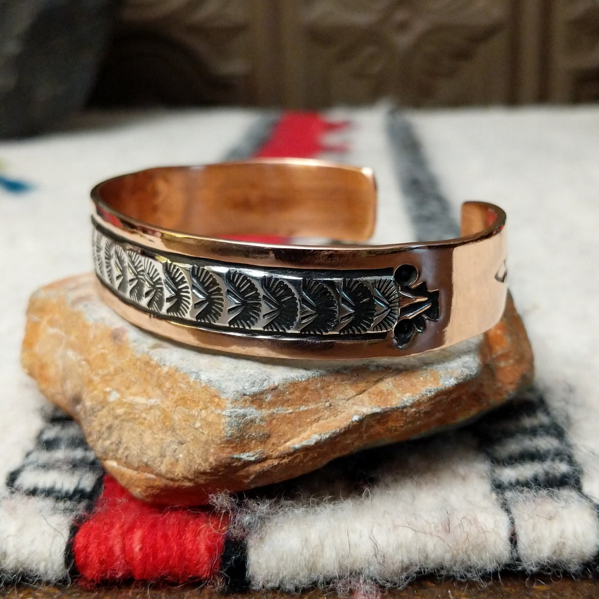 Copper and silver cuff by Robert Little featuring a repeating oxidized hand-stamped design across the silver center, framed by polished copper borders; side view.