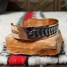 Copper and silver cuff by Robert Little featuring a repeating oxidized hand-stamped design across the silver center, framed by polished copper borders; side view.