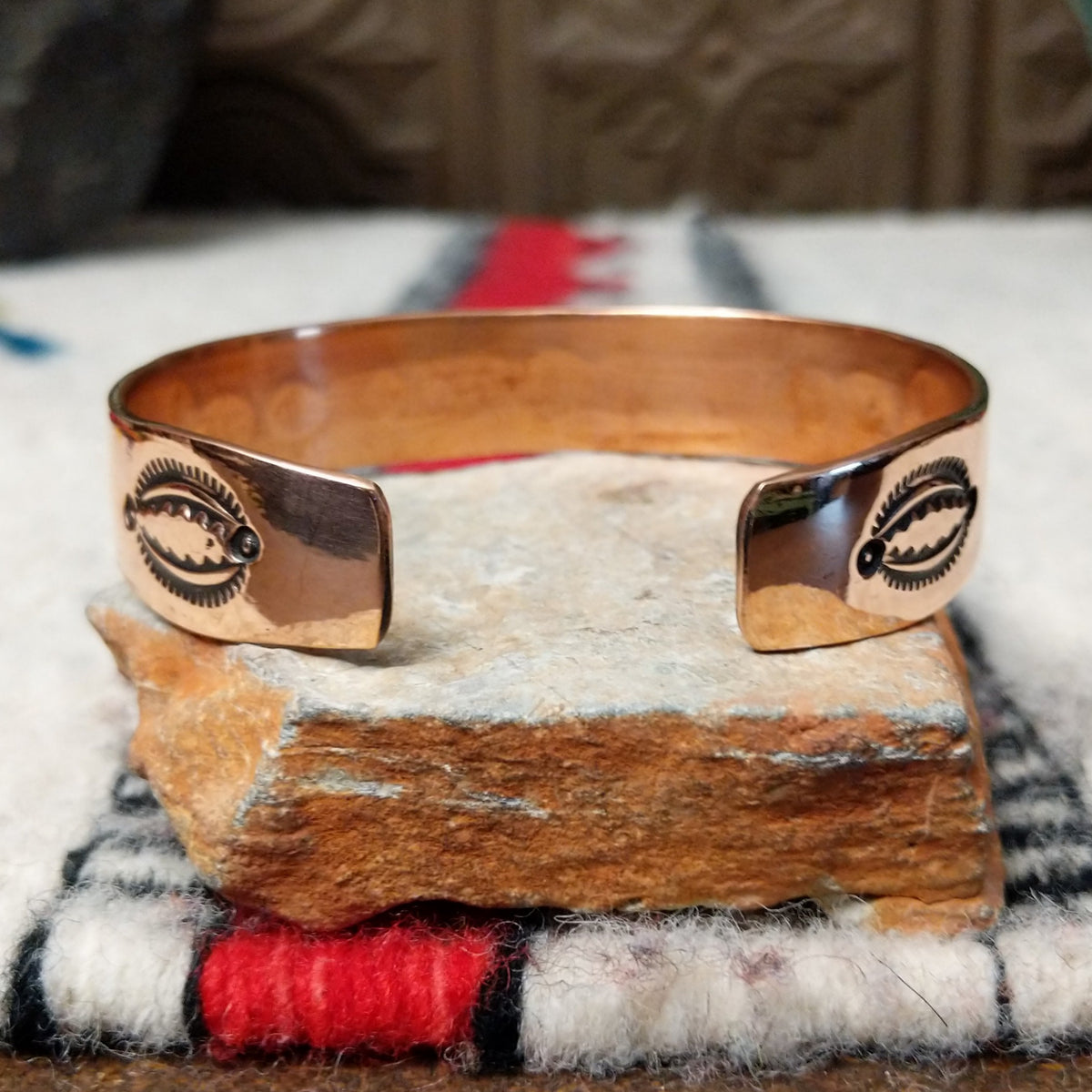 This Copper & Silver Cuff by Robert Little features a polished copper band, sterling silver center, oxidized geometric stamping, and a central floral design; underside view.