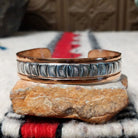 Copper and silver cuff by Robert Little featuring a repeating stamped ray design across an oxidized silver center, framed by polished copper borders.