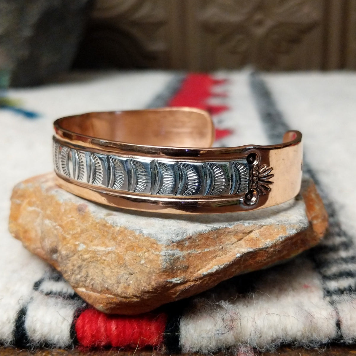 Copper and silver cuff by Robert Little featuring a repeating stamped ray design across an oxidized silver center, framed by polished copper borders; side view.