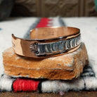 Copper and silver cuff by Robert Little featuring a repeating stamped ray design across an oxidized silver center, framed by polished copper borders; side view.