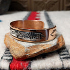 Copper and silver cuff by Robert Little featuring an intricate repeating hand-stamped geometric pattern with oxidized accents, framed by polished copper borders; side view.