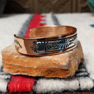 Copper and silver cuff by Robert Little featuring an intricate repeating hand-stamped geometric pattern with oxidized accents, framed by polished copper borders; side view.