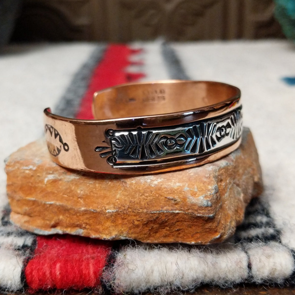 Copper and silver cuff by Robert Little featuring an intricate repeating hand-stamped geometric pattern with oxidized accents, framed by polished copper borders; side view.
