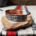 Copper and silver cuff by Robert Little featuring a repeating stepped geometric pattern in oxidized sterling silver, framed by polished copper borders; side view.