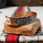 Copper and silver cuff by Robert Little featuring a repeating stepped geometric pattern in oxidized sterling silver, framed by polished copper borders; side view.