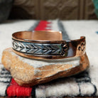 Copper and silver cuff by Robert Little featuring repeating stamped tipi-inspired geometric designs across an oxidized silver center, framed by polished copper borders.; side view.