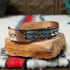 Copper and silver cuff by Robert Little featuring repeating stamped tipi-inspired geometric designs across an oxidized silver center, framed by polished copper borders; side view.