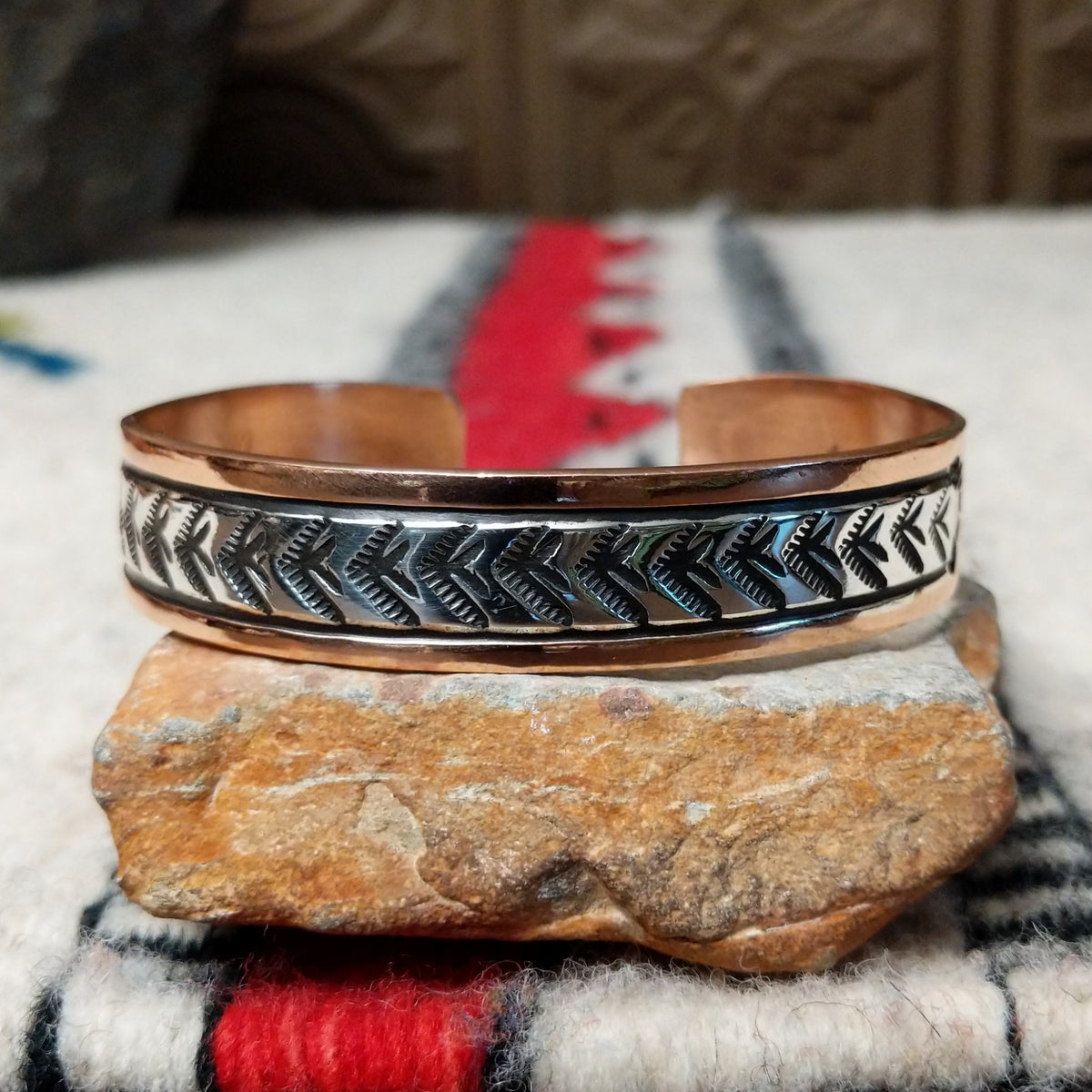 Copper and silver cuff by Robert Little featuring a repeating hand-stamped chevron or feather-inspired pattern with dark oxidized accents and polished copper borders.